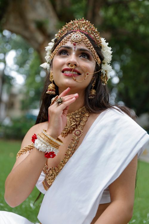 Free Portrait of an Indian woman wearing traditional attire with jewelry, sitting outdoors. Stock Photo