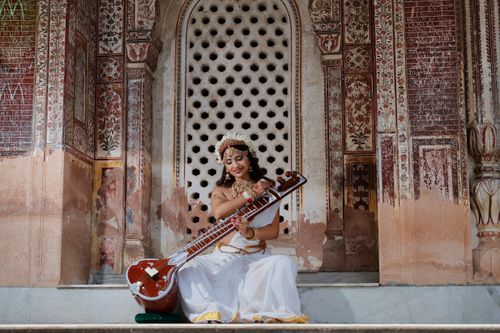 Free A woman dressed in traditional Indian attire playing a sitar at a historic architectural location. Stock Photo