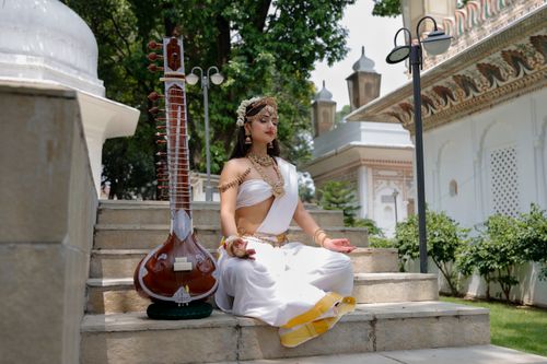 Free A woman in traditional attire meditates beside a veena on outdoor stone steps with temple backdrop. Stock Photo
