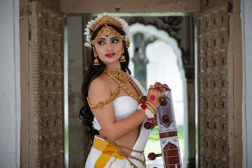 Free Portrait of an Indian woman in traditional attire and jewelry, holding a tanpura. Stock Photo