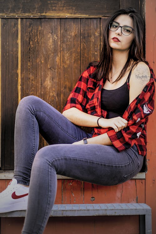 Free Woman in Red and Black Plaid Shirt and Blue Denim Jeans Sitting on Brown Wooden Bench Stock Photo