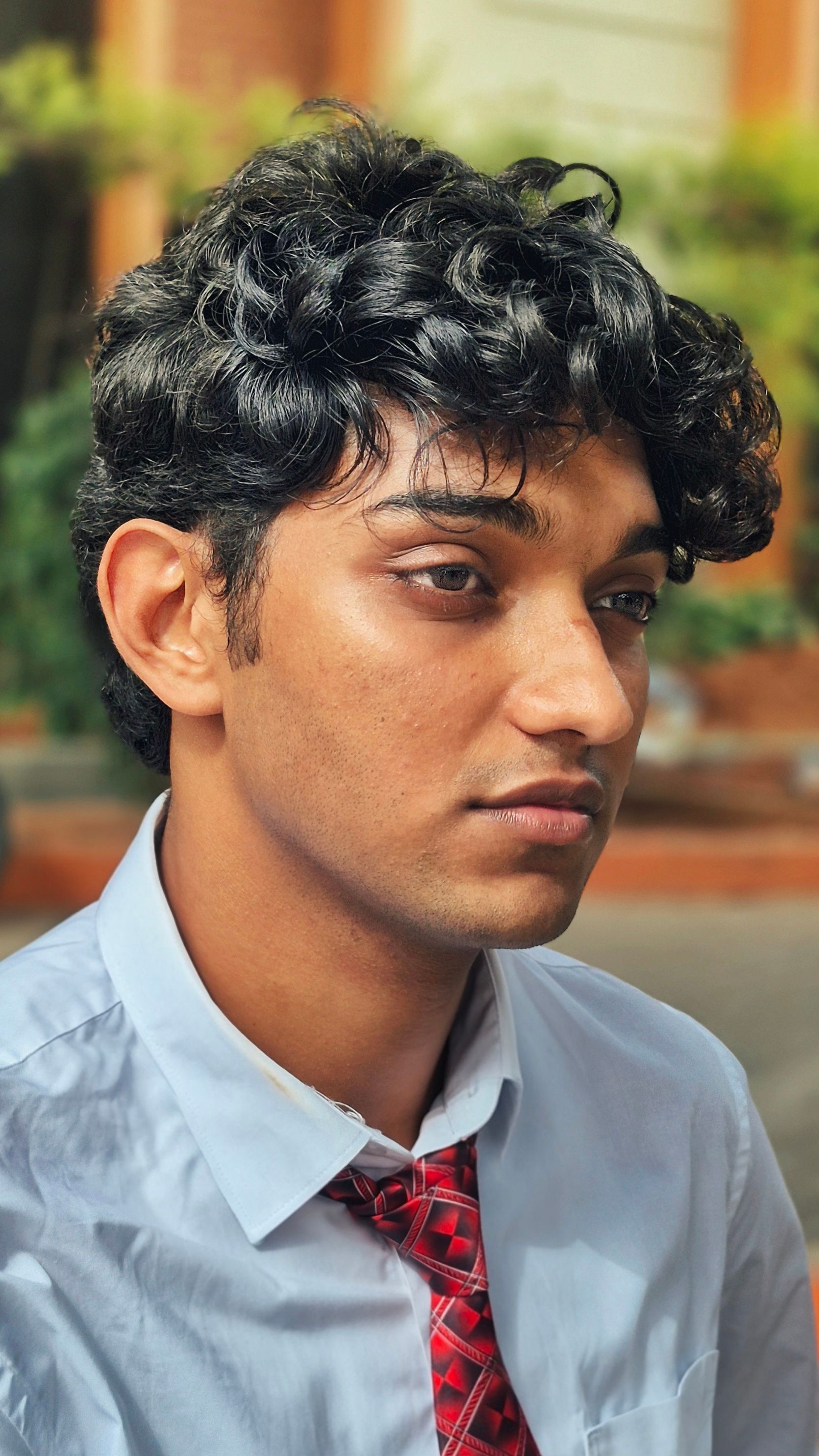 Portrait of a young man with curly hair wearing a tie, photographed outdoors on a sunny day.