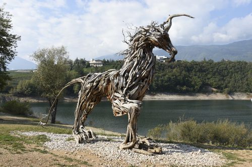 Free Majestic driftwood horse sculpture stands by a serene lake in Trentino-Alto Adige, Italy. Stock Photo