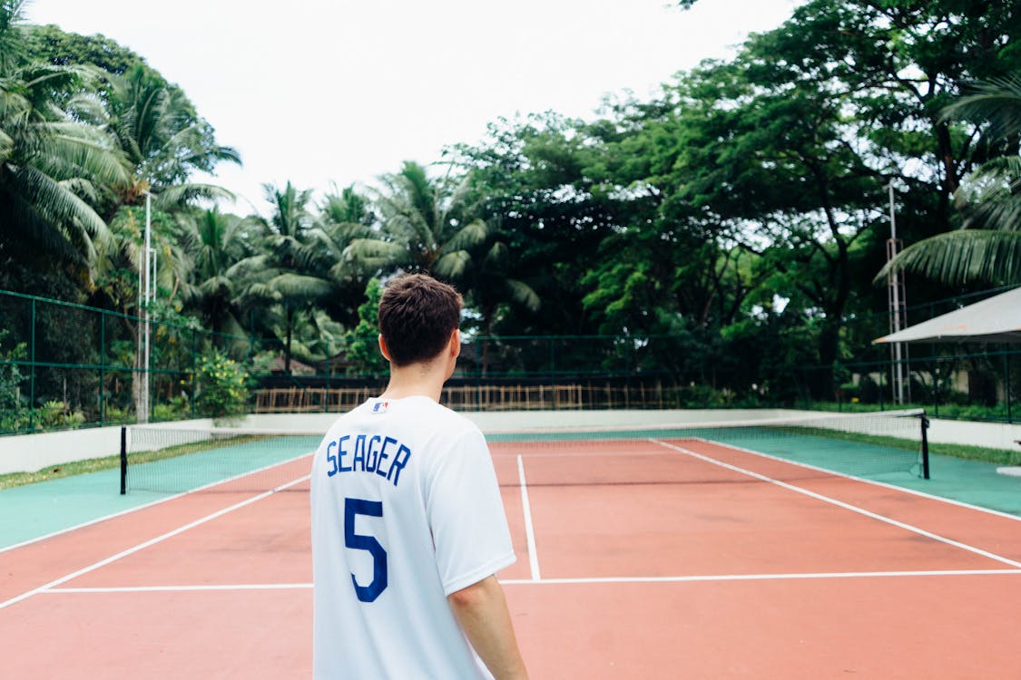 Free Man in White and Blue Jersey Shirt Standing on Tennis Court Stock Photo