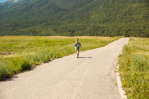 Free A happy child runs on a country path through lush greenery with mountains in the background. Stock Photo