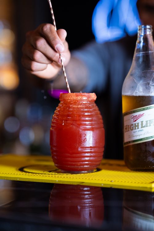 Free Close-up of a hand stirring a michelada cocktail next to a beer bottle at a bar. Stock Photo