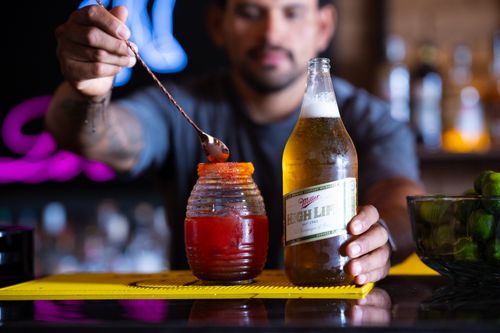 Free A bartender expertly prepares a michelada using Miller High Life beer in a vibrant bar setting. Stock Photo