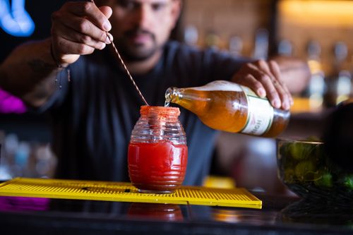 Free A bartender skillfully prepares a refreshing michelada with beer and tomato juice in a lively bar setting. Stock Photo