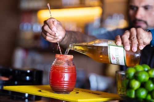 Free A bartender skillfully prepares a refreshing michelada with precise pouring technique in a vibrant bar setting. Stock Photo