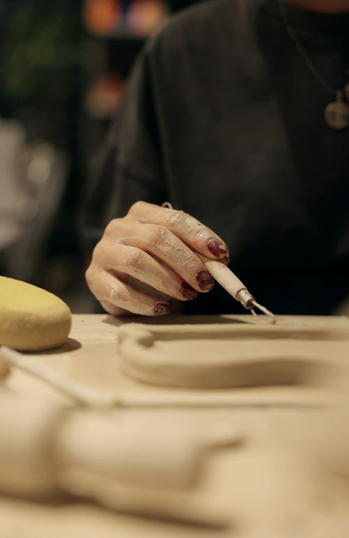 Free Close-up of an artist shaping clay with precision tools in a dimly lit workshop. Stock Photo