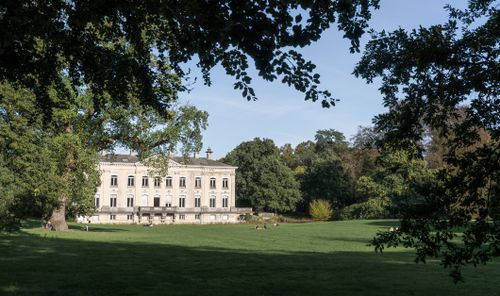 Free Charming neoclassical mansion with lush green garden, framed by vibrant autumn trees. Stock Photo