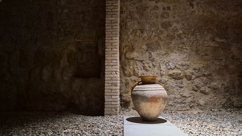Free Rustic stone wall with a solitary ancient clay pot, serene archaeological ambiance. Stock Photo
