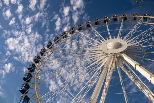 Free A stunning view of a Ferris wheel set against a vibrant blue sky with scattered clouds. Stock Photo