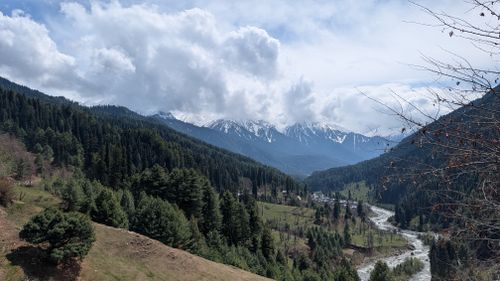Free Captivating view of snow-capped mountains, lush forest, and a winding river under a cloudy sky. Stock Photo