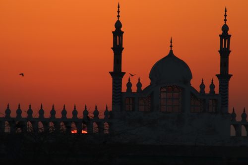 Free Mosque silhouette against a vibrant orange sunset sky, with birds flying nearby. Stock Photo