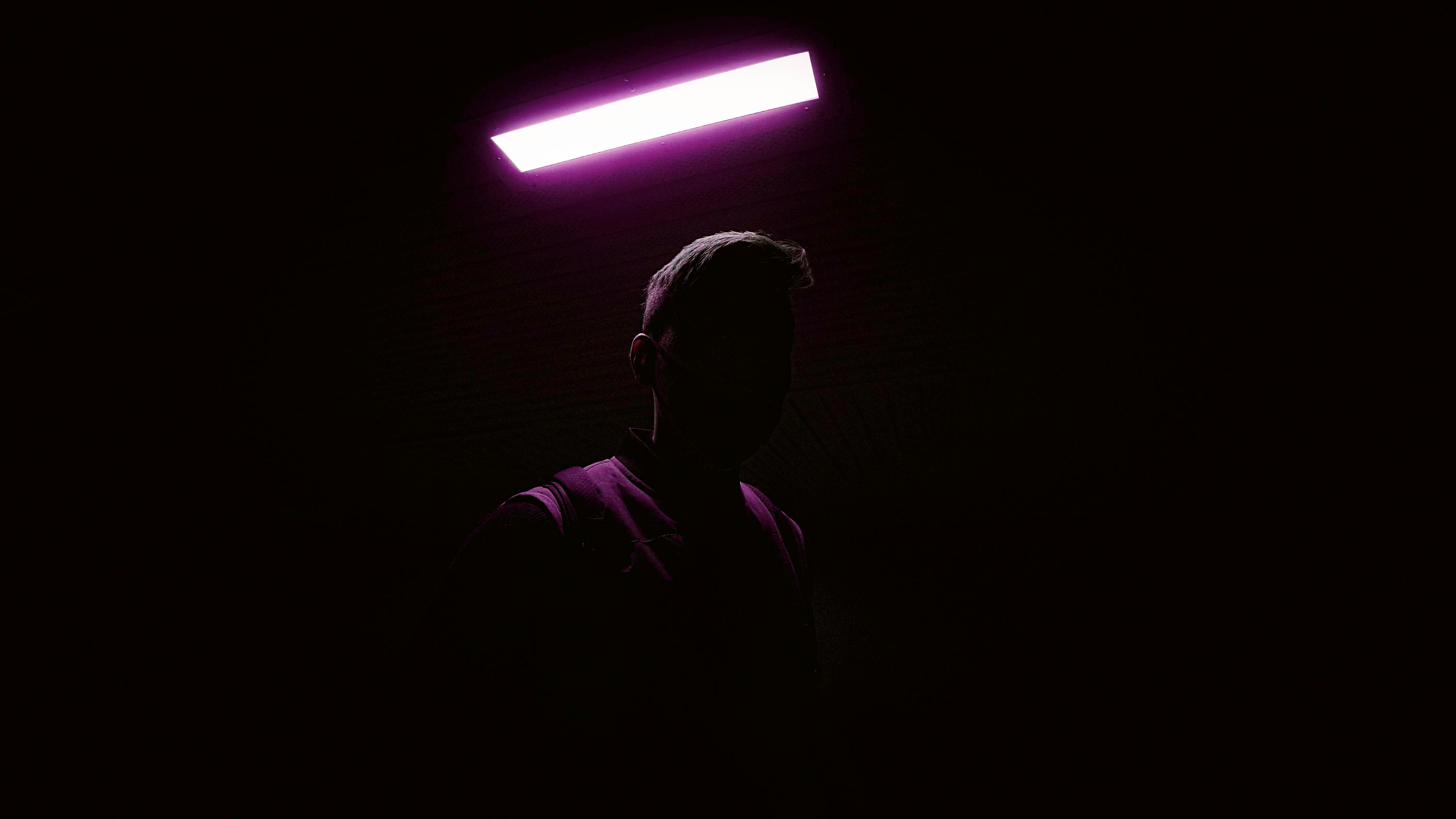 From below of anonymous hiding man standing under glowing lamp with pink neon