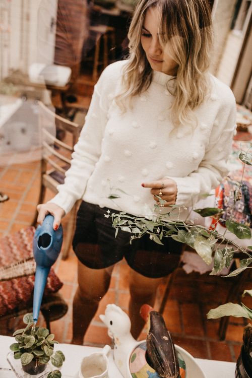 Free A woman indoors watering houseplants with a blue watering can. Casual and serene setting. Stock Photo