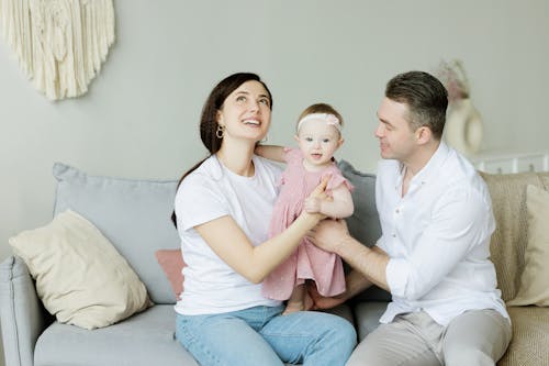 Man in White Long Sleeve Shirt Sitting Beside Woman in White T-shirt Holding a Girl