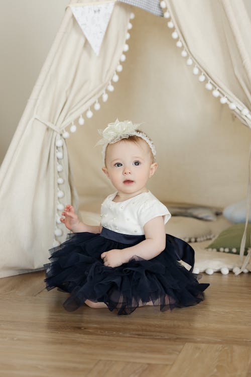 Girl in White and Black Dress Sitting on Brown Wooden Surface 