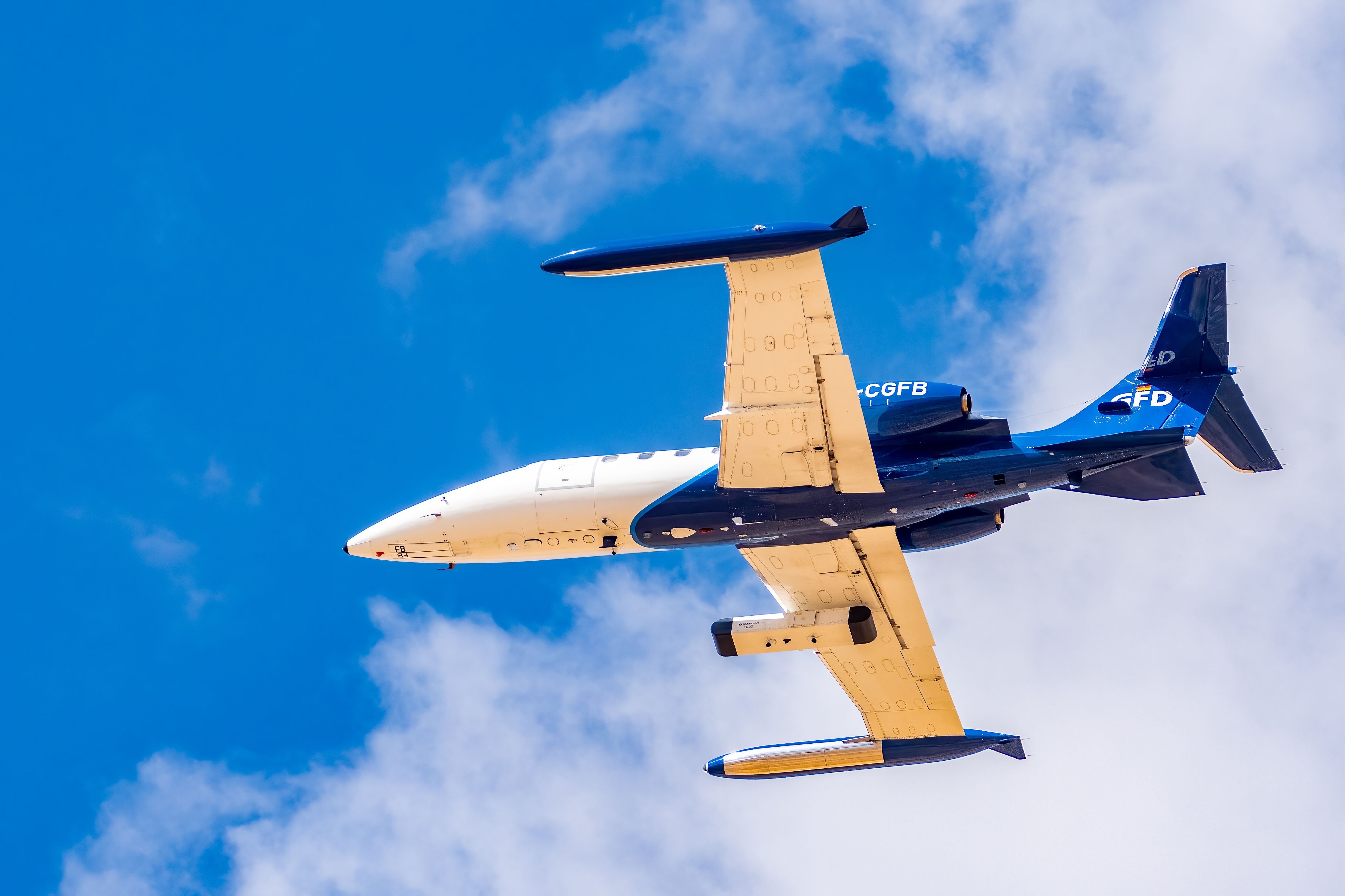 Specialty aircraft flying over Albacete, Spain against a bright blue sky.