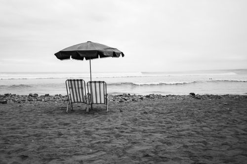 Free Classic black and white shot of beach chairs and umbrella on Trujillo's serene coast. Stock Photo