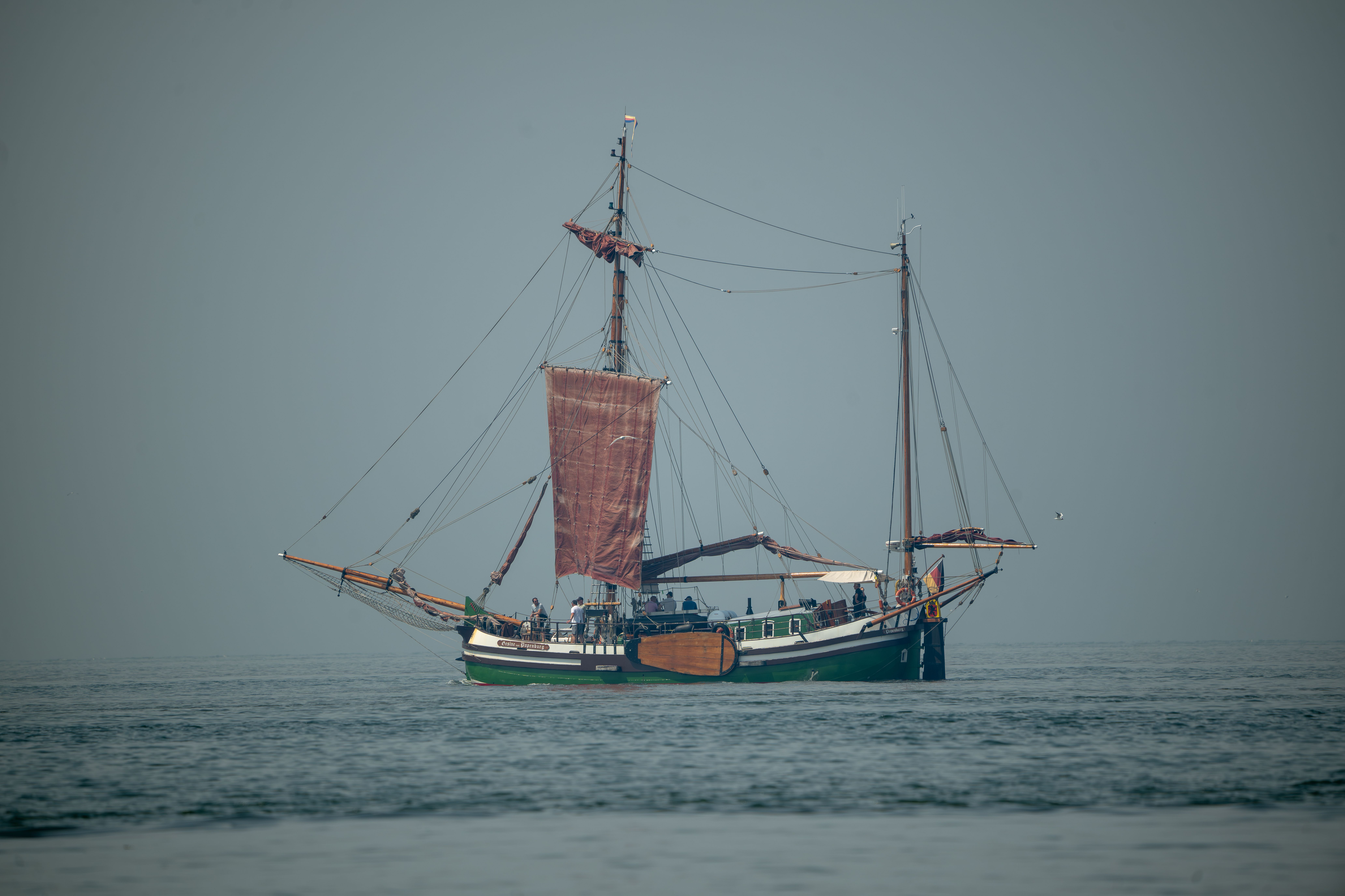 A classic sailing ship with red sails navigates calm open waters during the day.