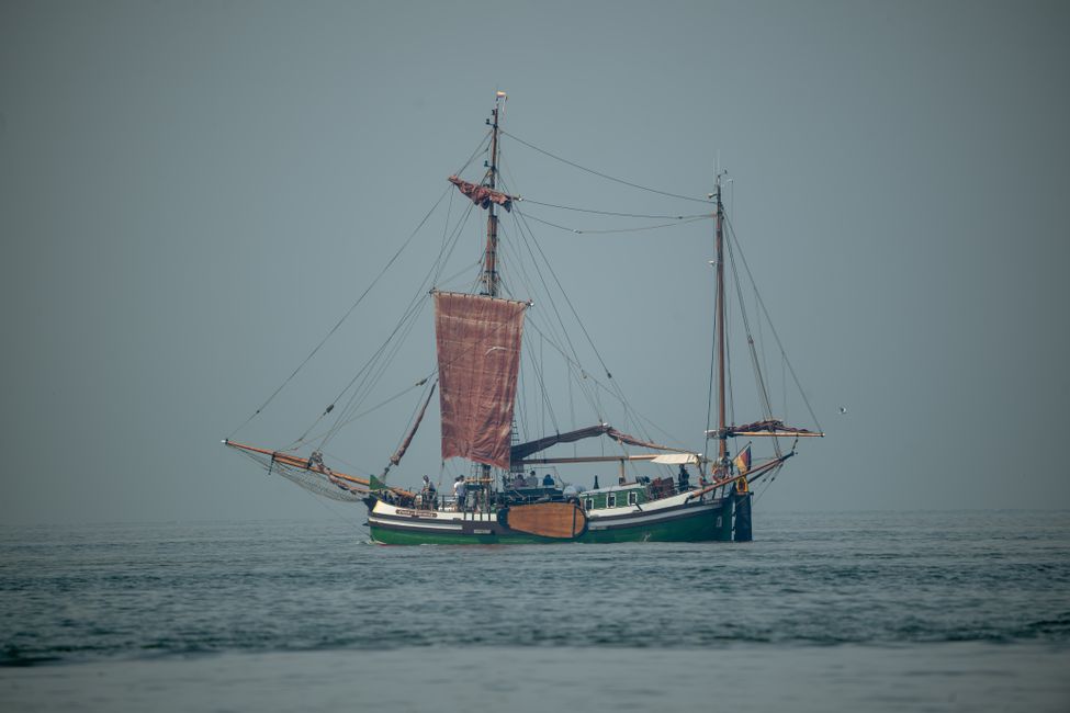 A classic sailing ship with red sails navigates calm open waters during the day.