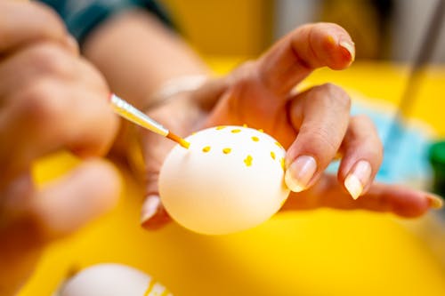 Person Decorating Easter Egg With Yellow Paint