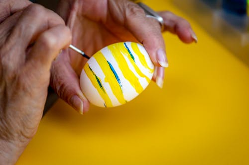 Free    Person Decorating White Egg With Yellow Paint Stock Photo