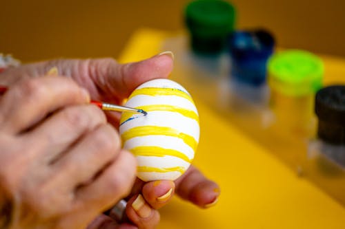 Person Decorating Easter Egg With Yellow Paint 