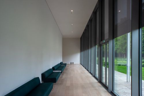 Free Spacious corridor with sleek design, featuring benches and wall-to-ceiling windows offering a garden view. Stock Photo