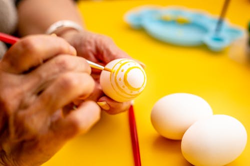 Person Painting White Egg With Yellow Paint