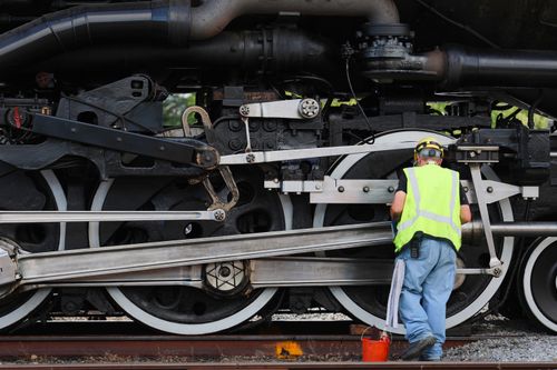 Free An engineer in a neon vest cleans the massive wheels of a historic steam locomotive outdoors. Stock Photo