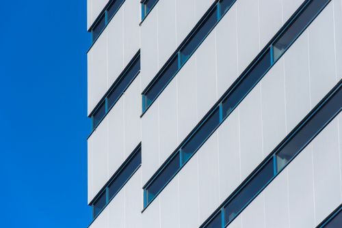 Free A minimalist view of a modern office building facade with diagonal lines against a clear blue sky. Stock Photo