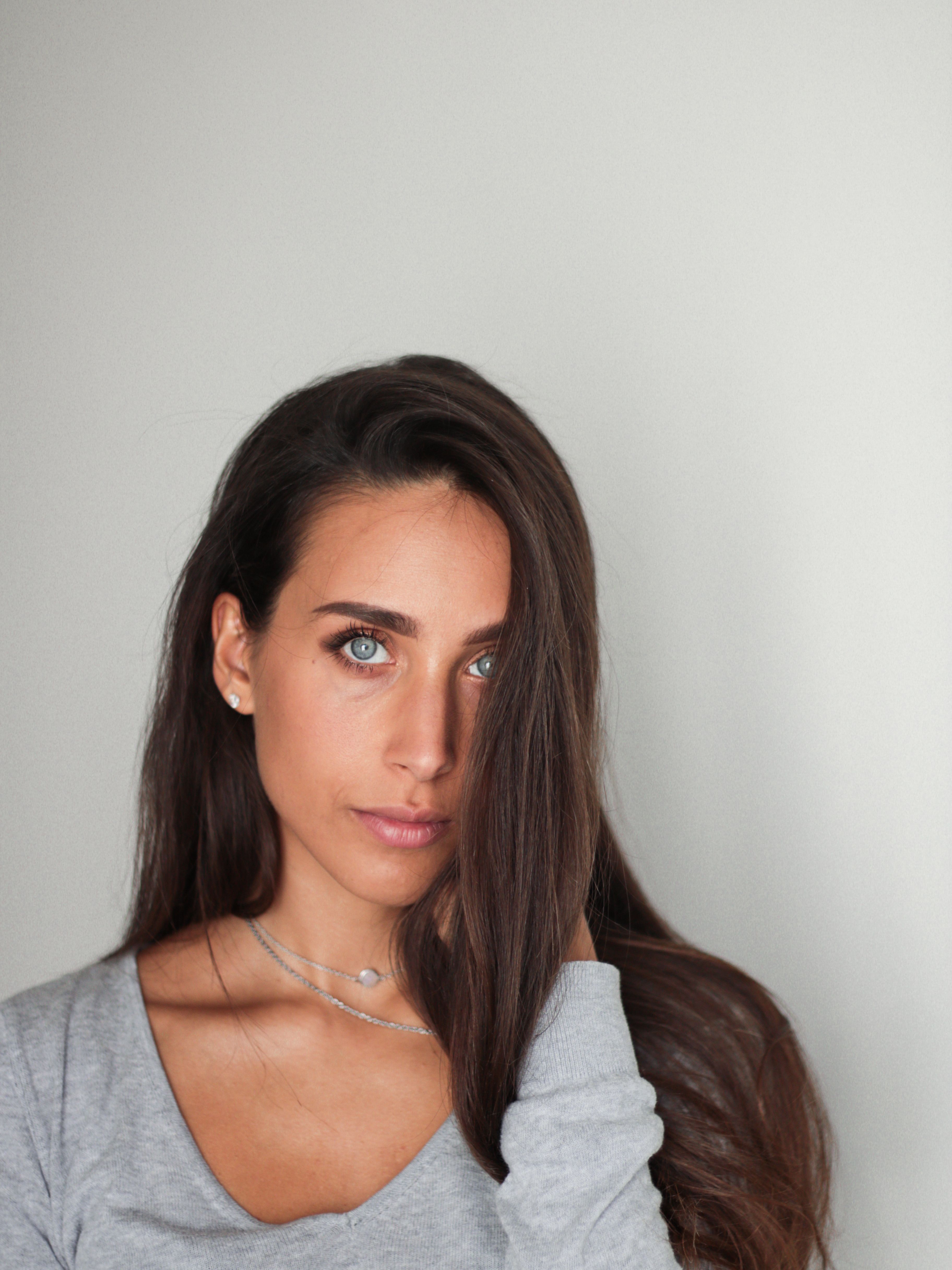 A portrait of a woman with long hair and striking blue eyes against a gray background.