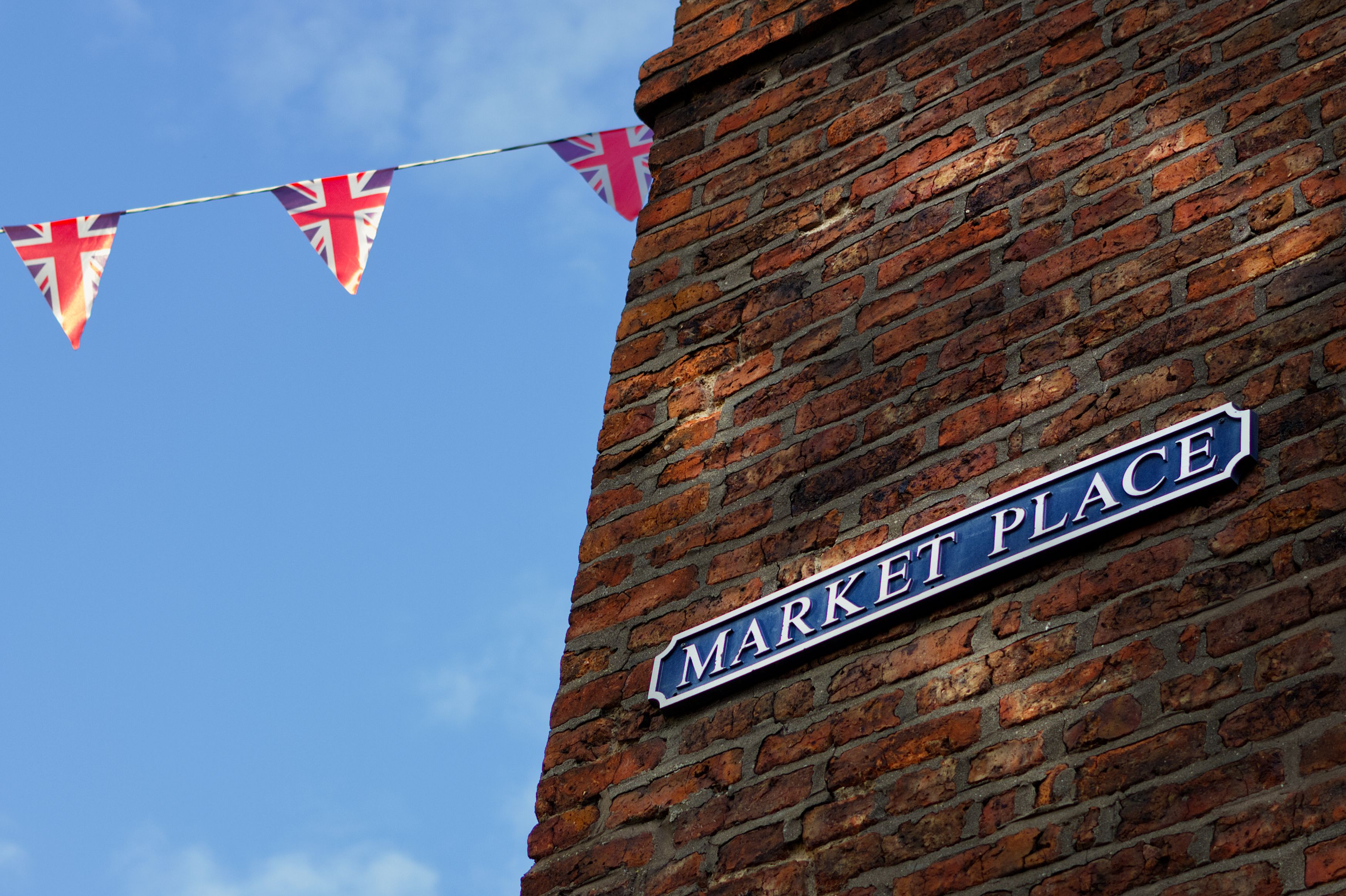 Brick wall with a Market Place sign in Morpeth, England, adorned with Union Jack bunting.