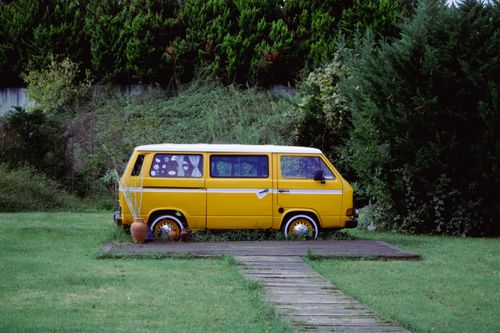 Free A vibrant yellow van parked on a grassy lawn surrounded by lush green trees in a serene outdoor setting. Stock Photo