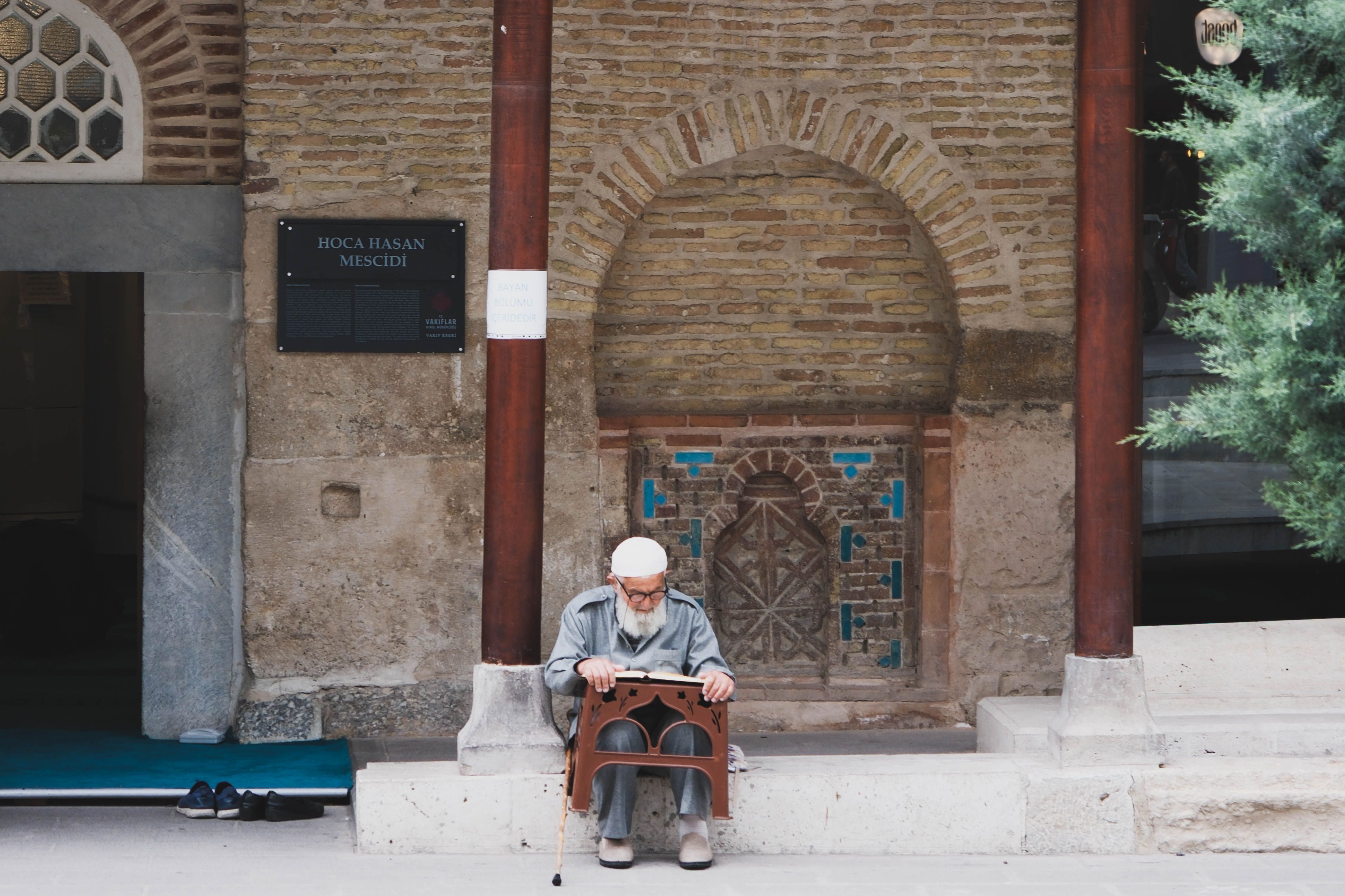 Senior man reading religious text outside the historic Hoca Hasan Mosque.