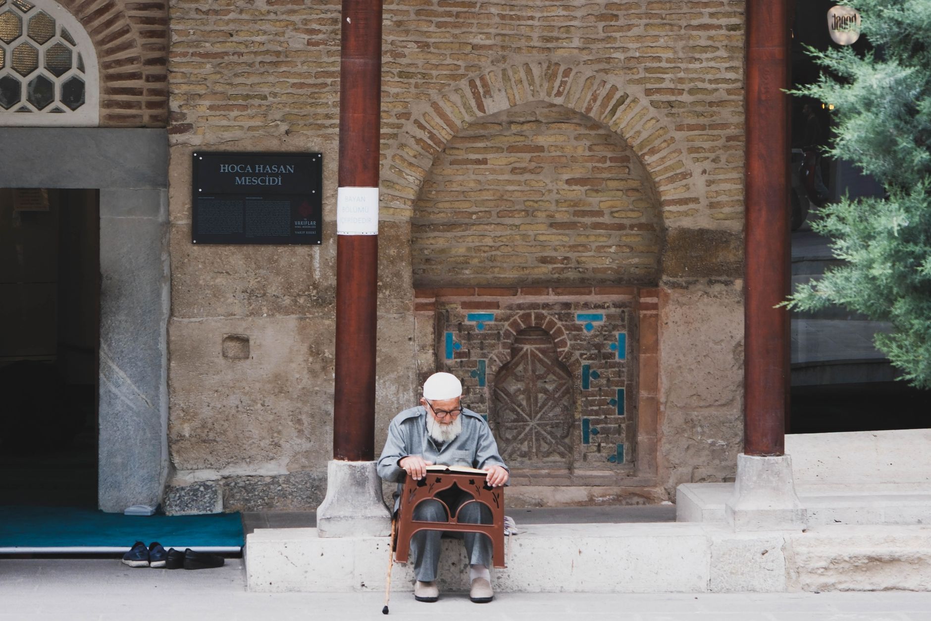 Senior man reading religious text outside the historic Hoca Hasan Mosque.