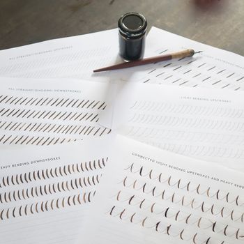 Overhead view of calligraphy practice sheets with an ink bottle and pen.（イメージ）