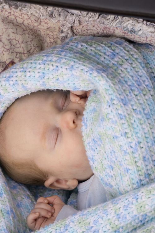 Free Newborn baby peacefully sleeping wrapped in a cozy pastel blanket, capturing serenity. Stock Photo