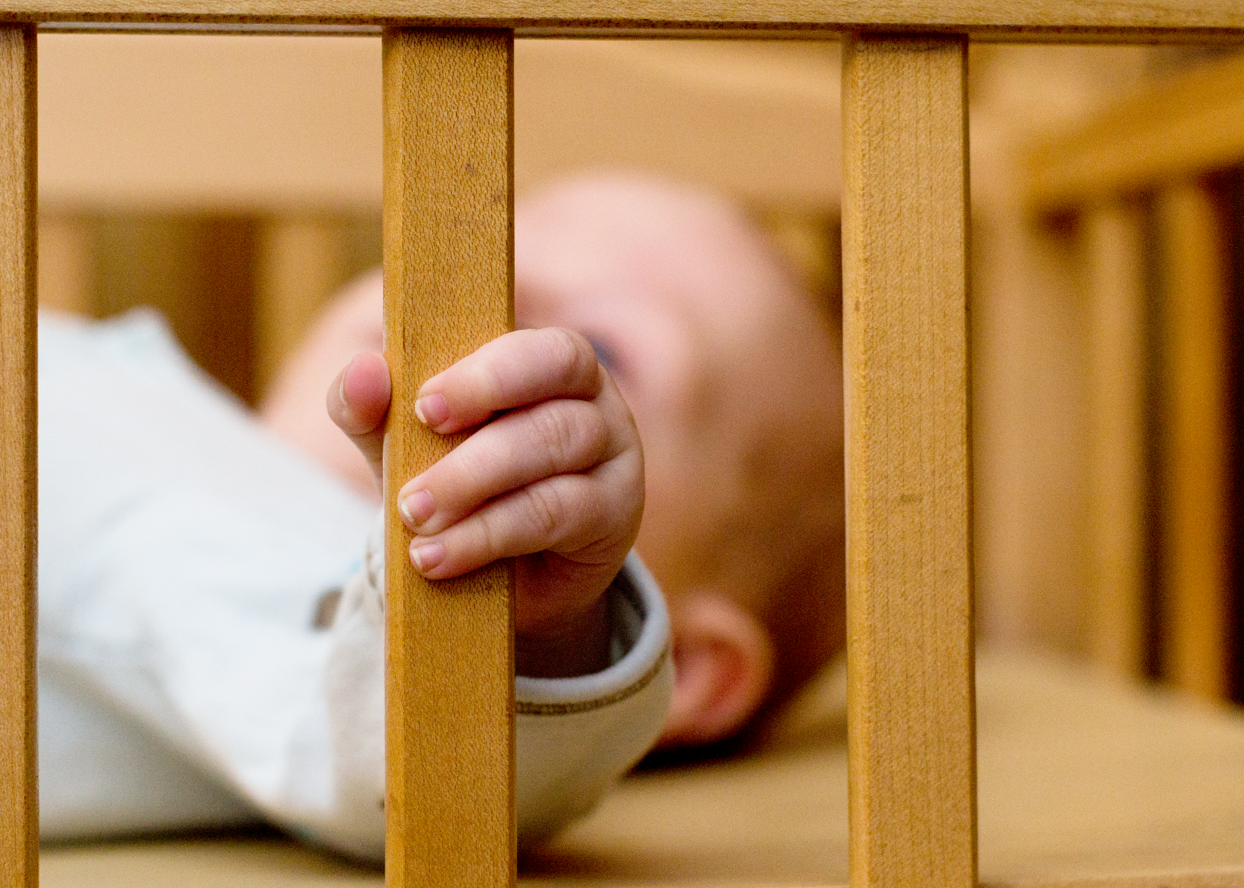 Closeup of a baby's hand holding a wooden crib rail, showcasing the innocence and gentleness of infants.