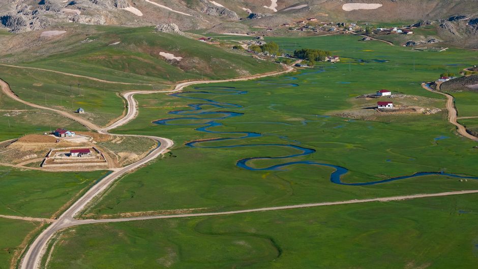 A stunning aerial capture of a winding river flowing through a lush green valley with scattered buildings.