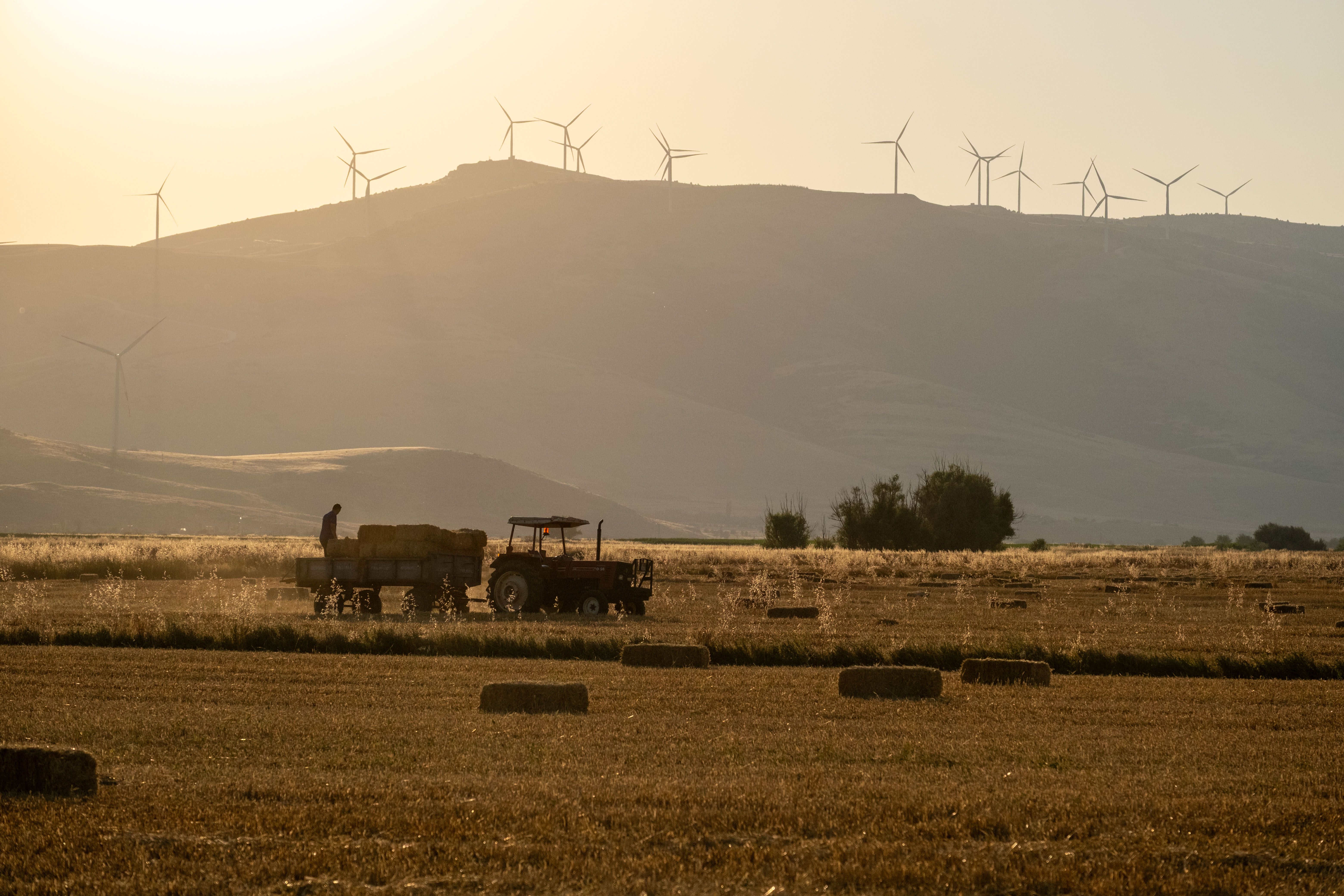 Tractor working in a field with wind turbines at sunset, symbolizing sustainable agriculture.