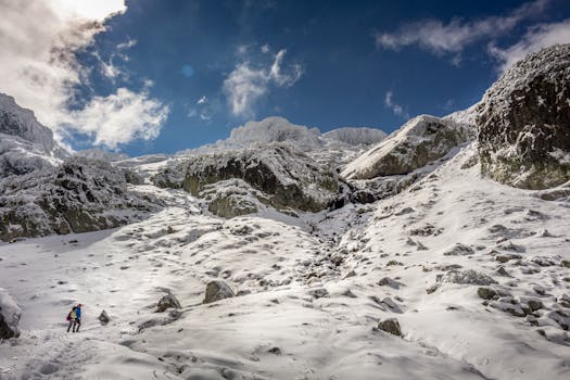 A lone climber ascends a snow-covered mountain under a bright blue sky.