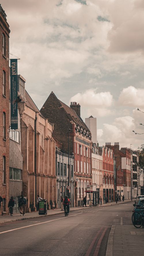 Free A scenic street view in London, featuring historic architecture and a bicycle rider, under a cloudy sky. Stock Photo