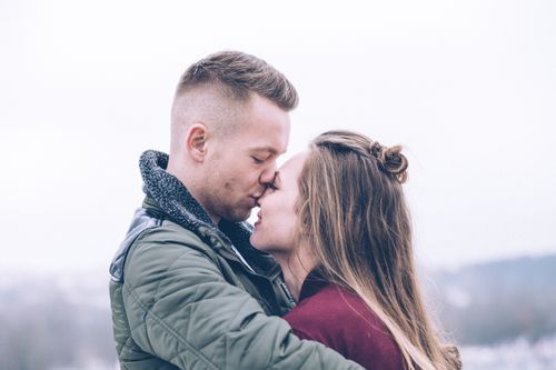 Free A romantic couple kisses outdoors on a chilly day, conveying warmth and affection. Stock Photo