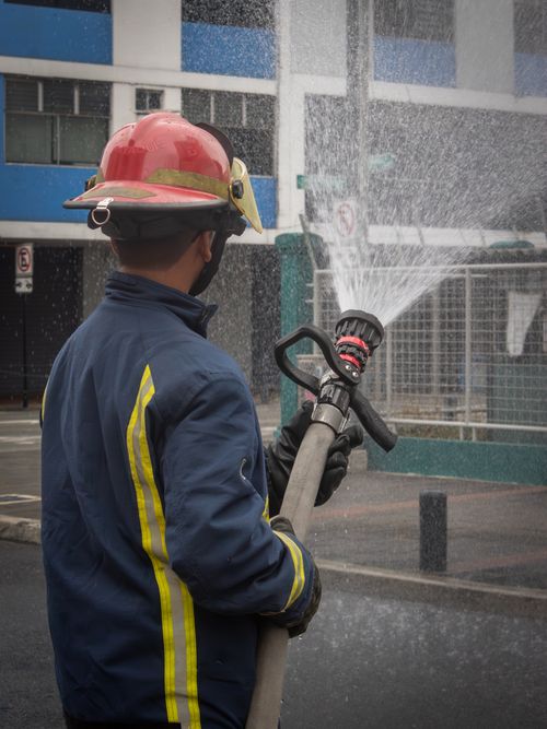 Free Firefighter in protective gear operates a hose during a training exercise outdoors. Stock Photo