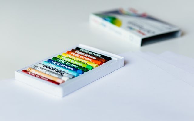 A small open box of Pentel oil pastels on a white table