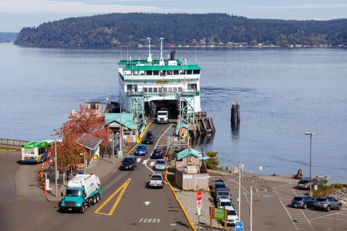 Free View of a Washington State Ferry docking at Bainbridge Island during the day with autumn foliage. Stock Photo